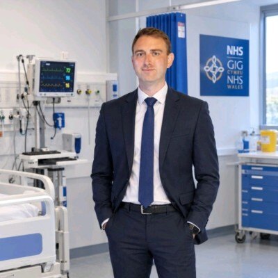 Luke Ashill in a suit, standing in a clinical skills room