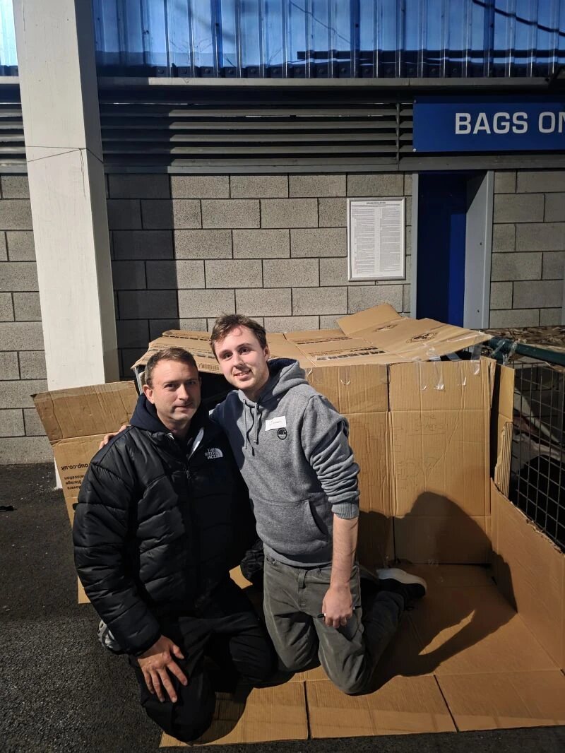 Luke and a fellow fundraiser kneeling in their cardboard shelter at the Big Sleep Out